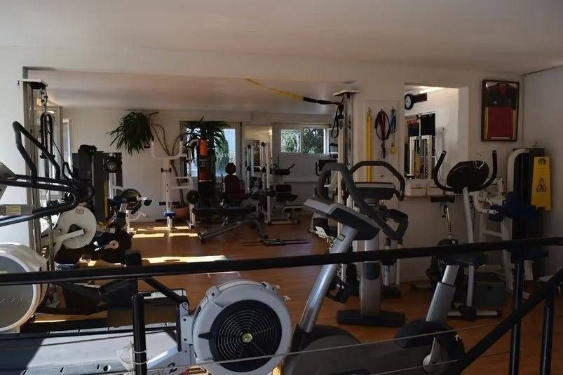Intérieur d'une salle de sport avec divers appareils de musculation, lumière naturelle et une personne utilisant un équipement.