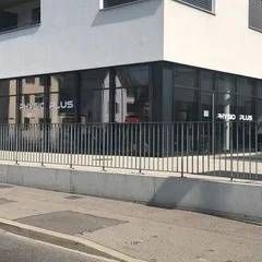 Clinique Physio Plus avec fenêtres en verre, façade blanche et barrière métallique.