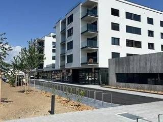 Immeuble d'appartements moderne blanc avec balcons, commerces au rez-de-chaussée, ciel bleu.