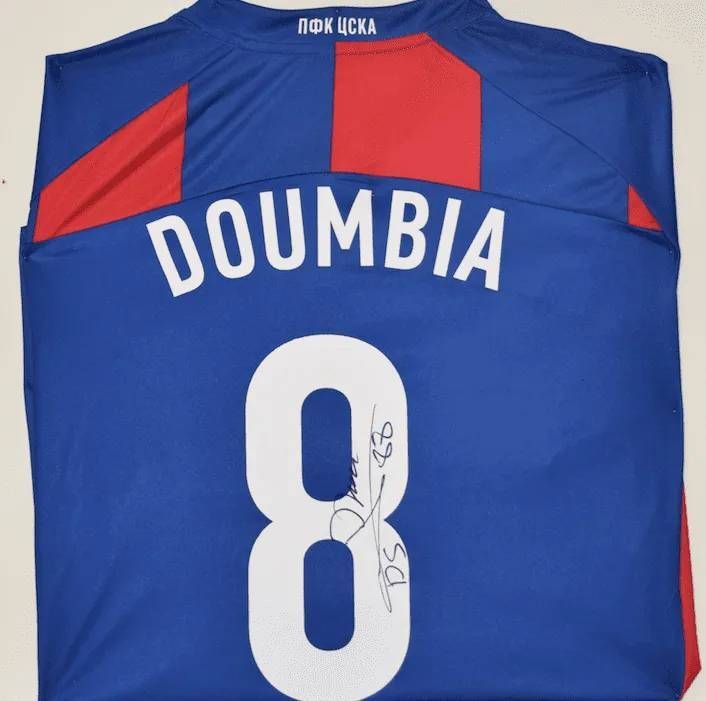 Maillot de football bleu avec l'inscription « DOUMBIA » et le numéro « 8 », signé à l'encre blanche ; empiècements rouges et bleus aux épaules.