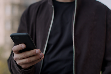 Un hombre con una chaqueta negra sostiene un teléfono celular en su mano.
