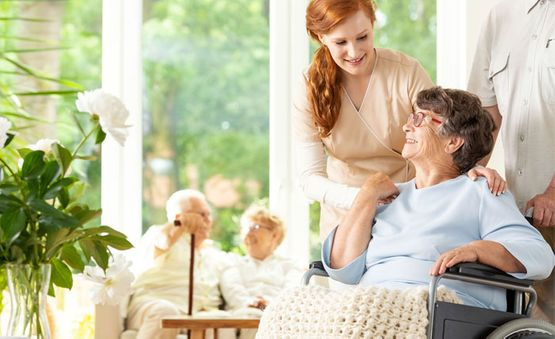 Una mujer está de pie junto a una anciana en silla de ruedas.