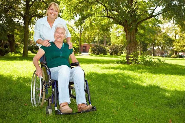 Una mujer está sentada junto a una mujer mayor en silla de ruedas en un parque.