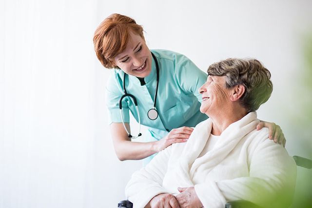 Una enfermera está hablando con una mujer mayor en silla de ruedas.