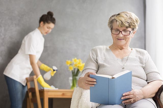 Una mujer mayor está sentada en una silla leyendo un libro.