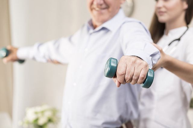 Una enfermera está ayudando a un anciano a hacer ejercicio con mancuernas.