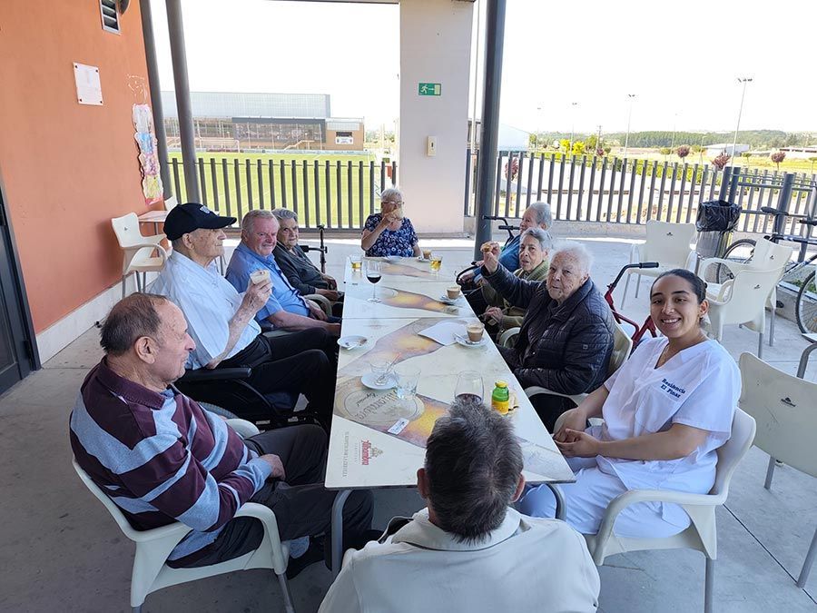 Varias personas sentadas alrededor de una mesa en un patio cubierto al aire libre, compartiendo una comida y una conversación.