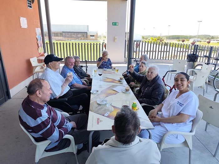 Varias personas sentadas alrededor de una mesa en un patio cubierto al aire libre, compartiendo una comida y una conversación.