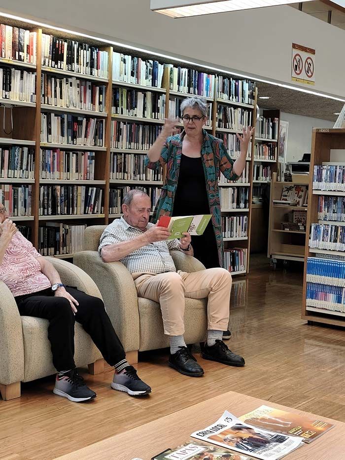 Gente sentada y de pie en una biblioteca, leyendo y hojeando libros.