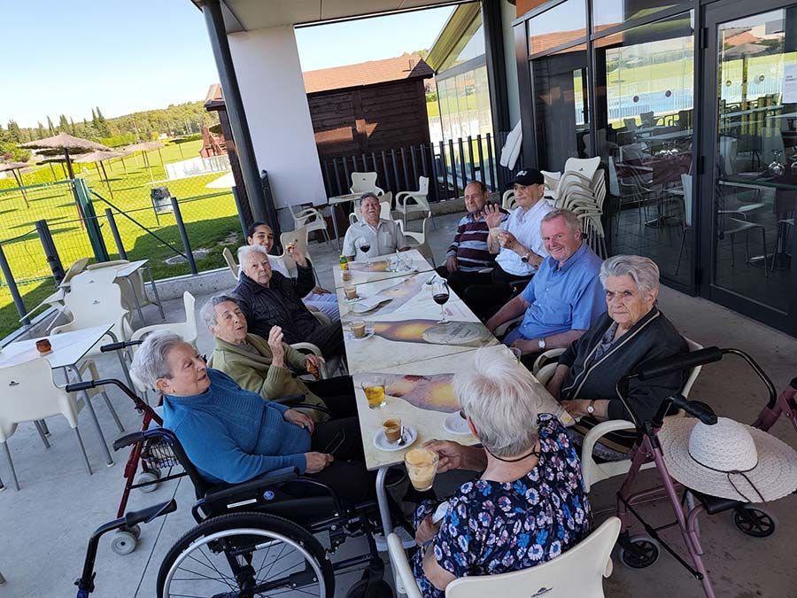 Gente sentada en una mesa de una cafetería al aire libre, charlando y tomando algo juntos en un patio cubierto.