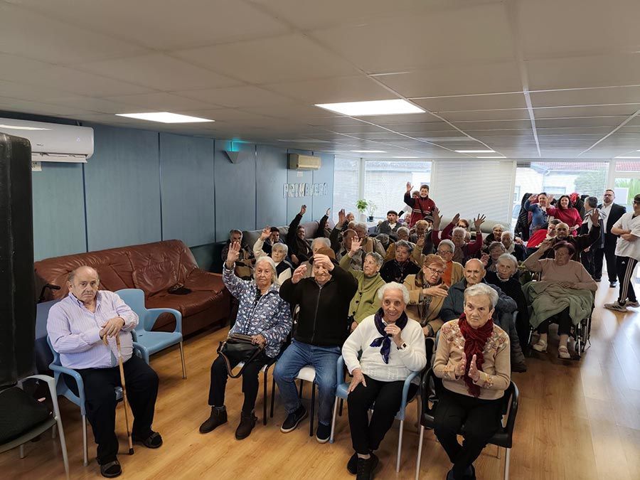 Sala comunitaria abarrotada de asistentes sentados, muchos de ellos con las manos levantadas, en una luminosa reunión en el interior.