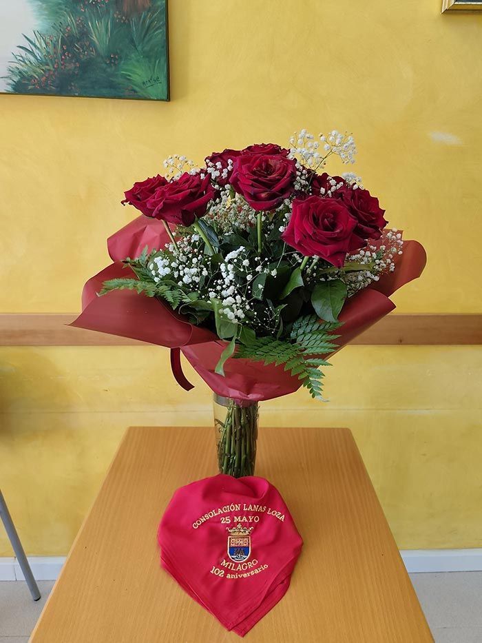 Ramo de rosas rojas en un jarrón sobre una mesa, con una tarjeta roja en forma de corazón delante.