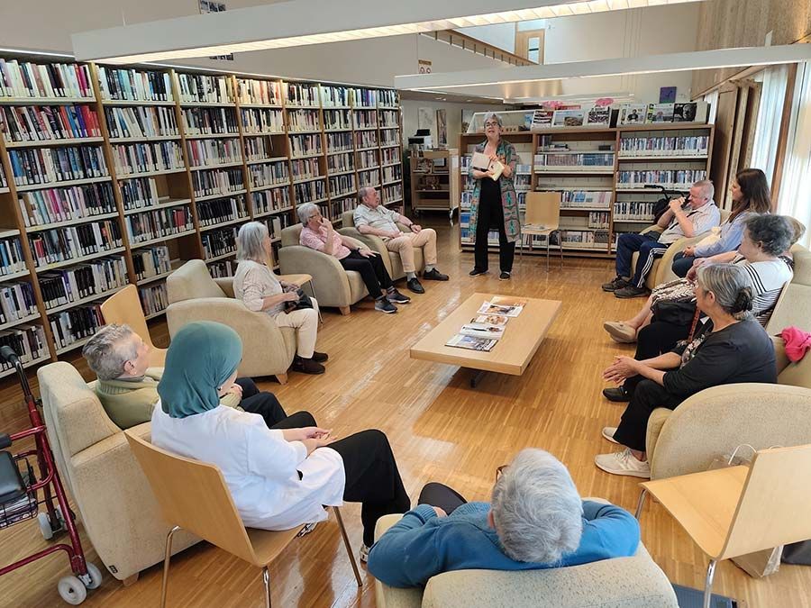 Personas sentadas en una biblioteca escuchando a un orador que se encuentra de pie cerca de las estanterías.