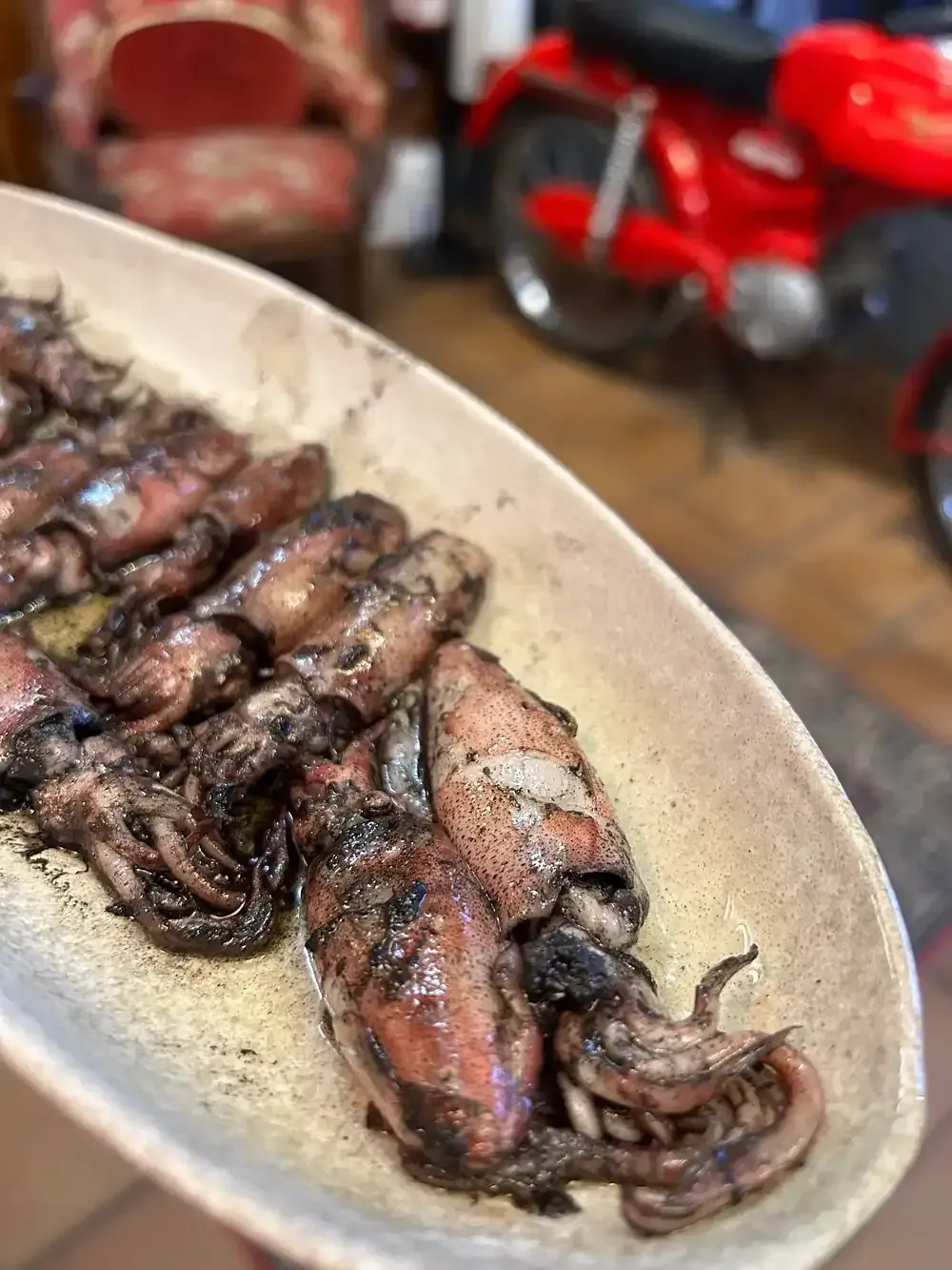 Calamares a la plancha en un plato ovalado y alargado. Al fondo, se ve una motocicleta roja desenfocada.