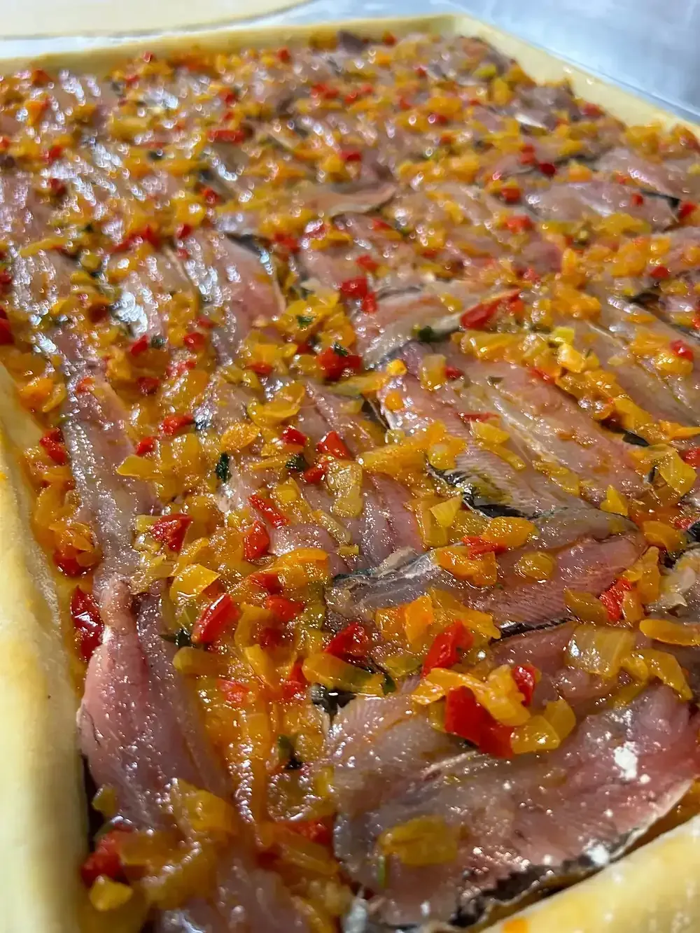 Tarta de anchoas y verduras. Anchoas con pimientos rojos y amarillos picados y cebolla sobre una base de hojaldre.