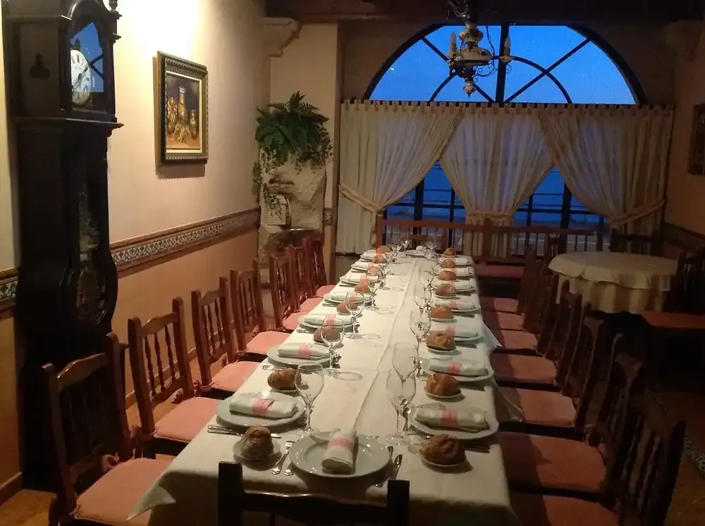 Mesa de comedor larga para comer en una habitación con una gran ventana y un reloj de pie.