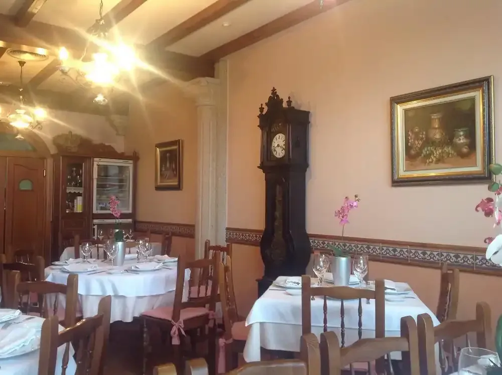 Interior de restaurante con mesas redondas dispuestas para cenar, reloj antiguo y obras de arte en la pared.