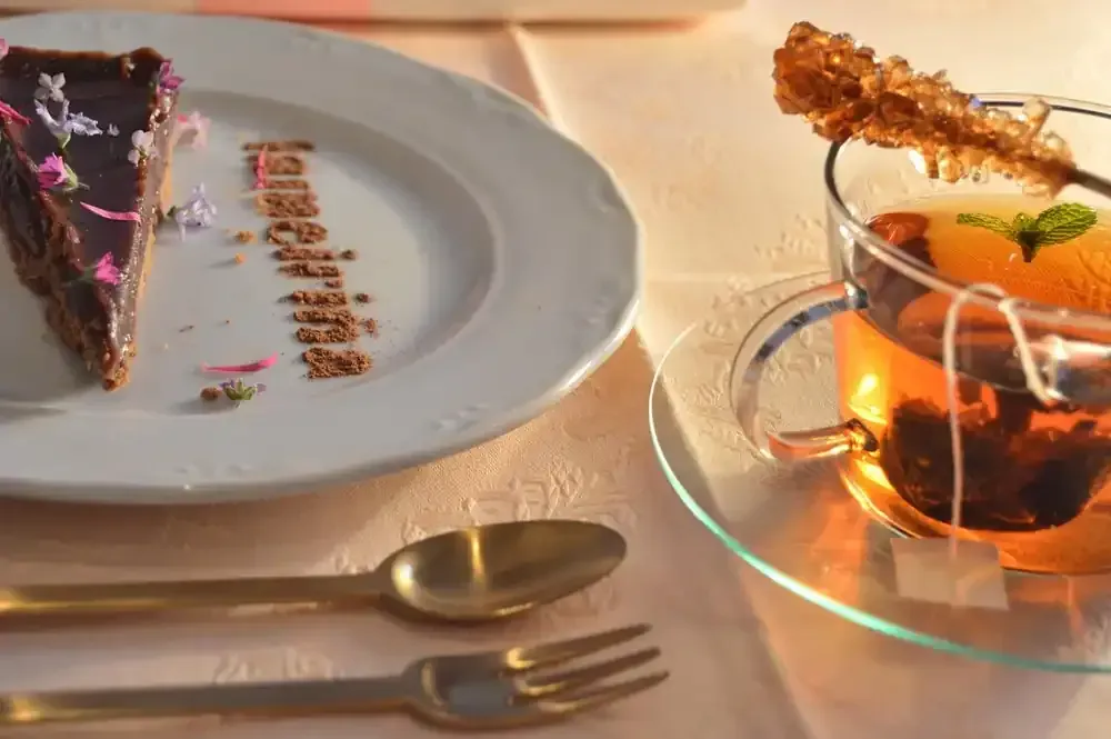 Rebanada de pastel de chocolate, té con caramelo de roca y cubiertos sobre una mesa.