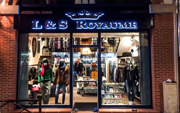 Façade du magasin L&S Royaume avec un extérieur en briques, une enseigne au néon et des présentoirs de vêtements et d'accessoires.