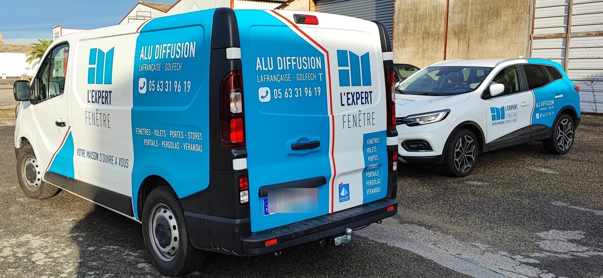 Une camionnette blanche et un SUV blanc ornés de motifs géométriques bleus et de logos d'entreprises sont garés sur un terrain gravillonné.