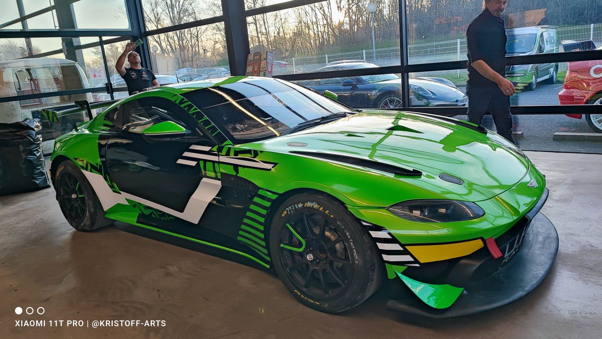 Une Aston Martin de course verte et noire est exposée dans un showroom, une personne se tenant à proximité.
