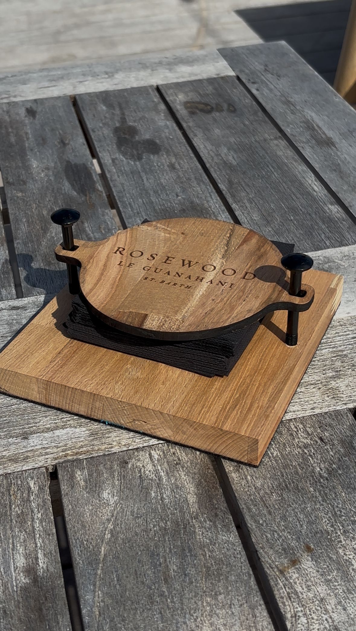Un petit sous-verre en bois avec l'inscription MID/WOOD gravée dessus, monté sur une base carrée en bois maintenue par quatre chevilles en métal noir.
