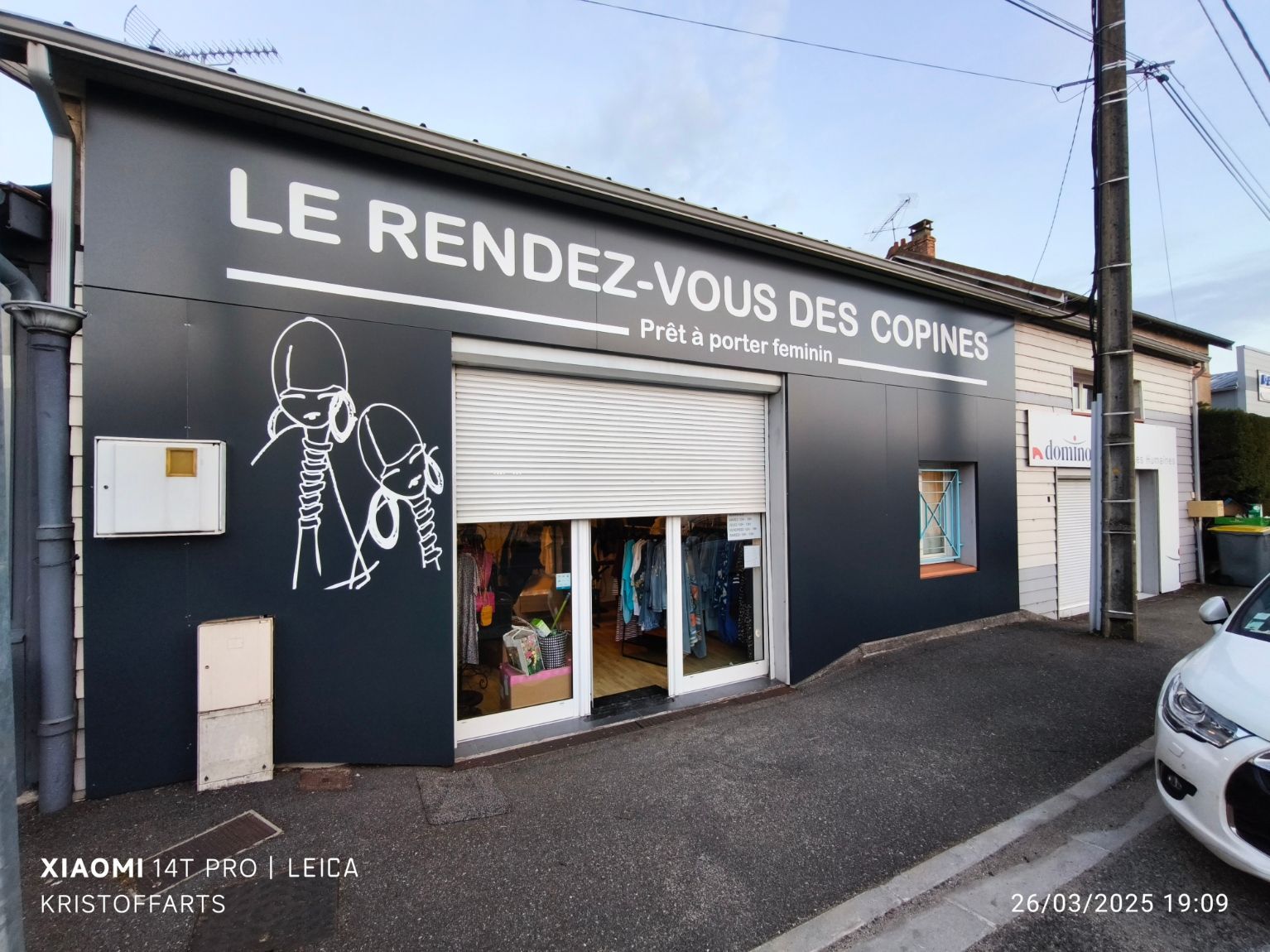 Une devanture de magasin appelée Le Rendez-Vous Des Copines, avec une façade noire et un dessin au trait blanc représentant deux personnes sur la gauche.