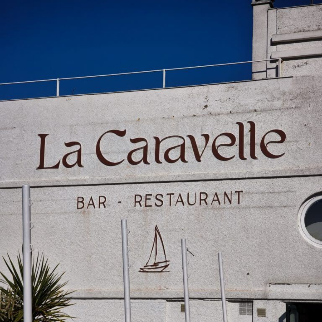 Façade blanche d'un bâtiment avec l'inscription La Caravelle - BAR - RESTAURANT et un petit dessin de voilier.