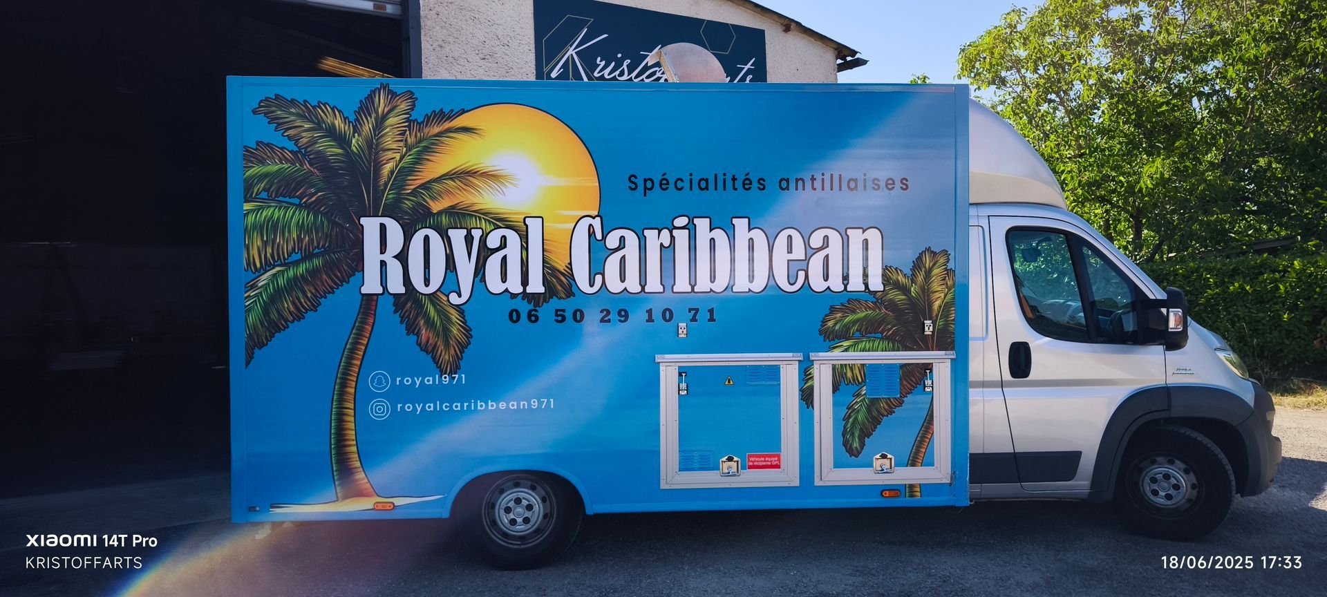 Un camion-restaurant blanc stationné à l'extérieur, recouvert d'une bâche publicitaire bleue représentant un palmier, un soleil et l'inscription Royal Caribbean.