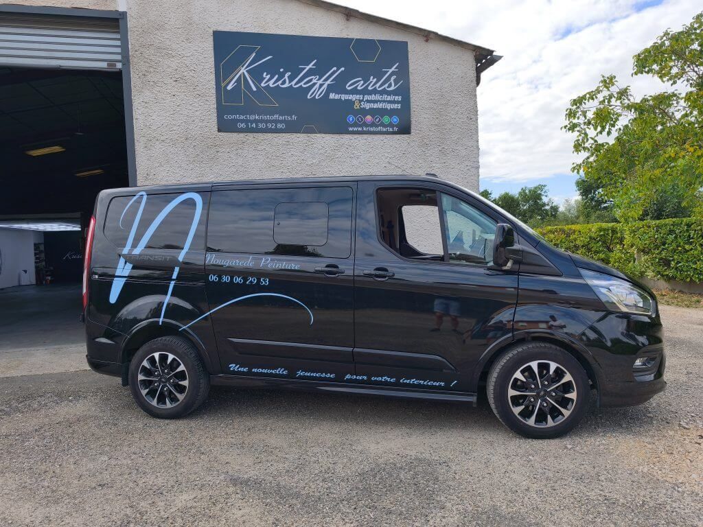 Une camionnette commerciale noire est garée devant un bâtiment portant l'enseigne Kristoff Arts sur sa façade.