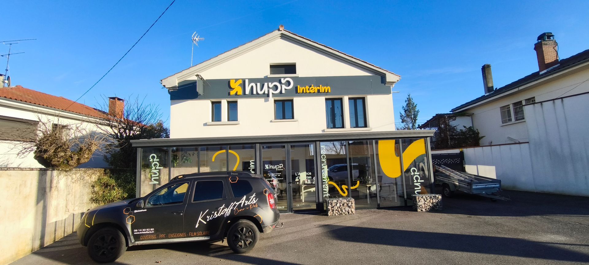 Un bâtiment de deux étages avec une enseigne hupp, une vitrine et un SUV garé devant par une journée ensoleillée.