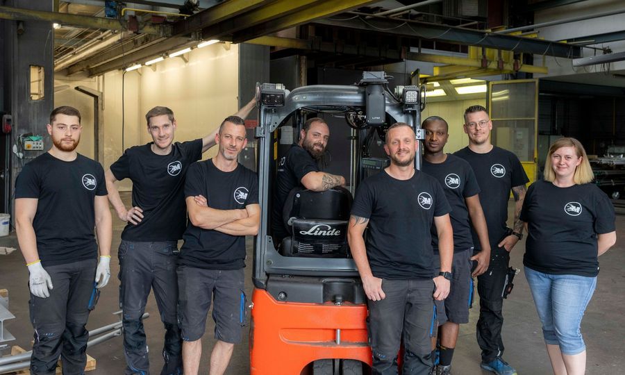 Eine Gruppe von Menschen posiert vor einem Gabelstapler für ein Foto.