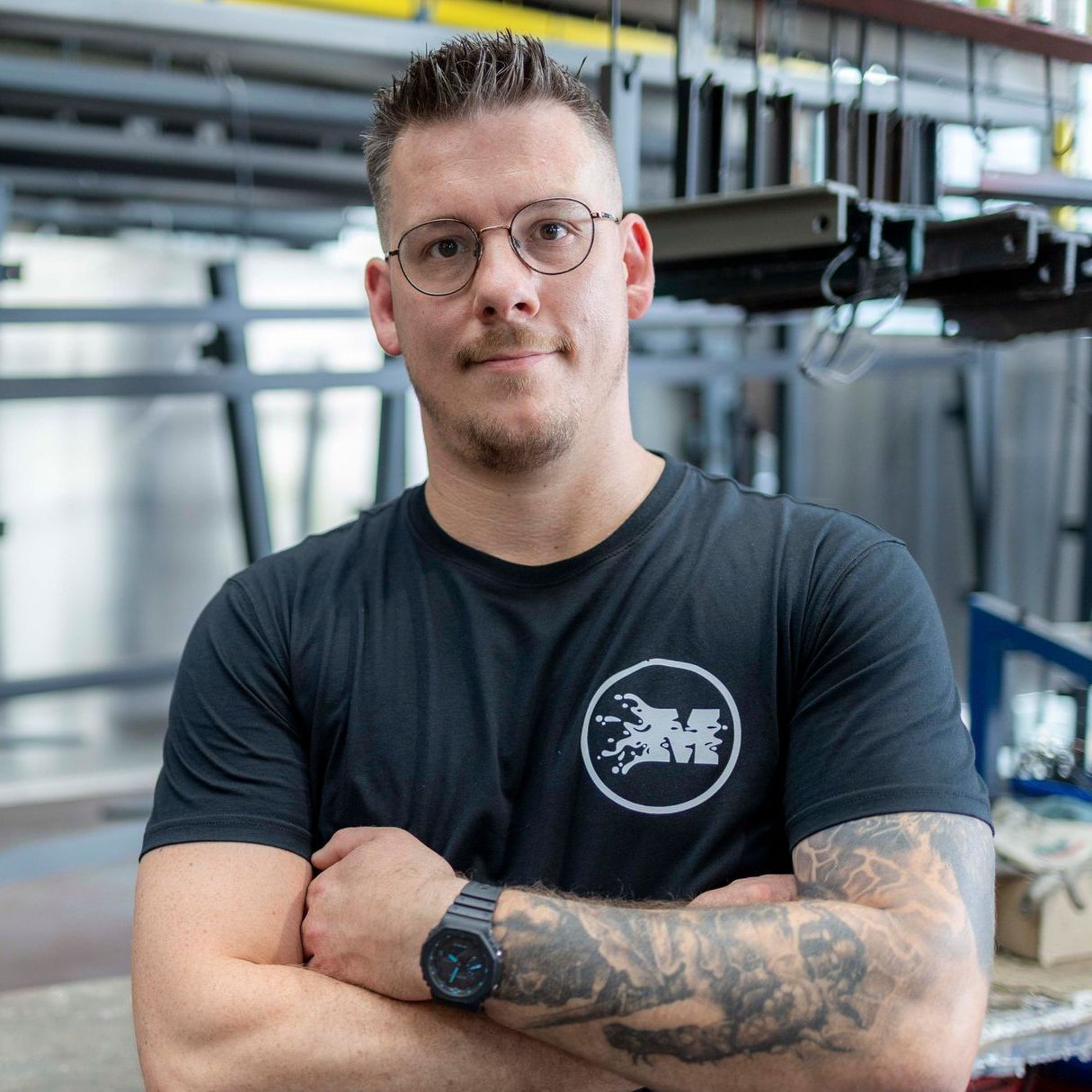 Ein Mann mit Brille und schwarzem Hemd mit dem Buchstaben M darauf