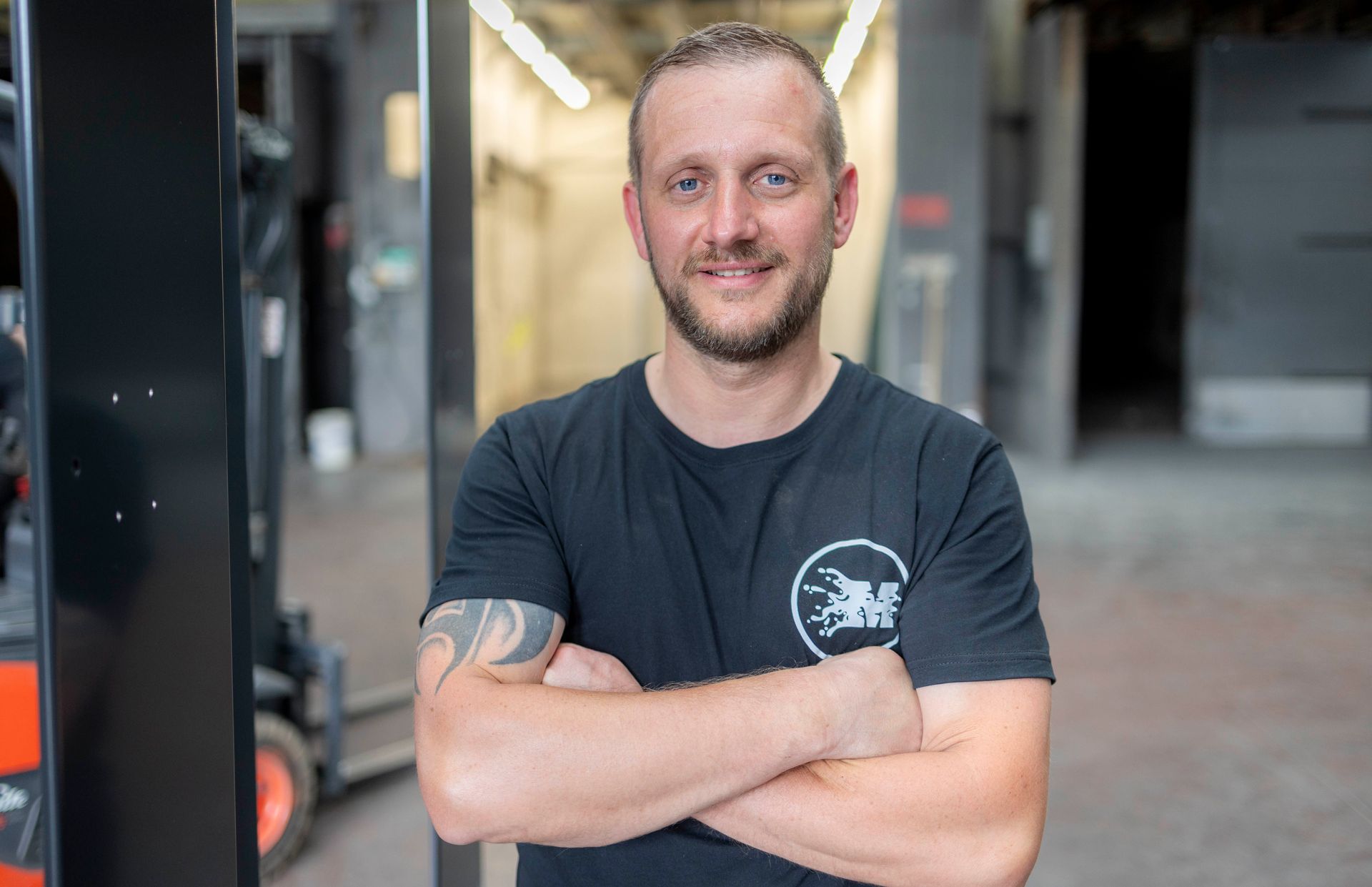 Ein Mann steht mit verschränkten Armen vor einem Gabelstapler in einem Lagerhaus.