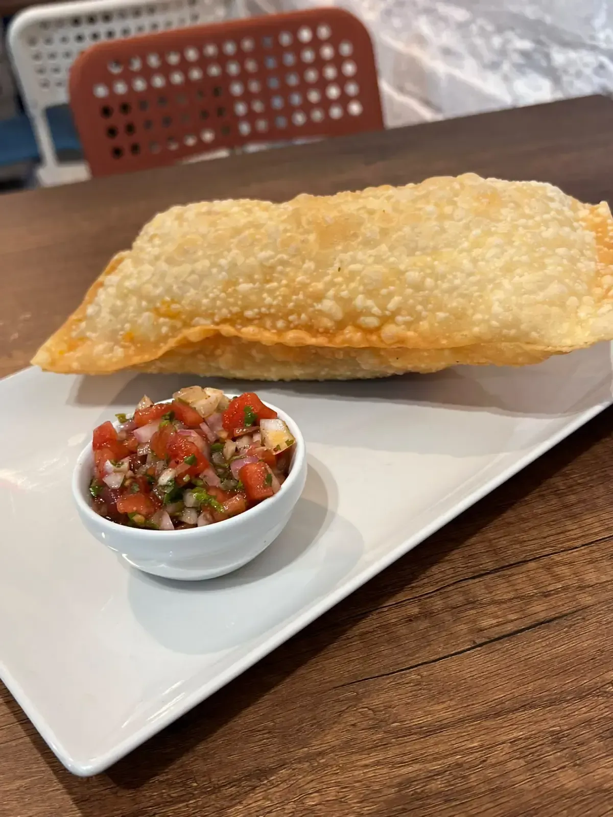 Pastel frito relleno en un plato blanco con una pequeña taza de salsa en una mesa de madera.