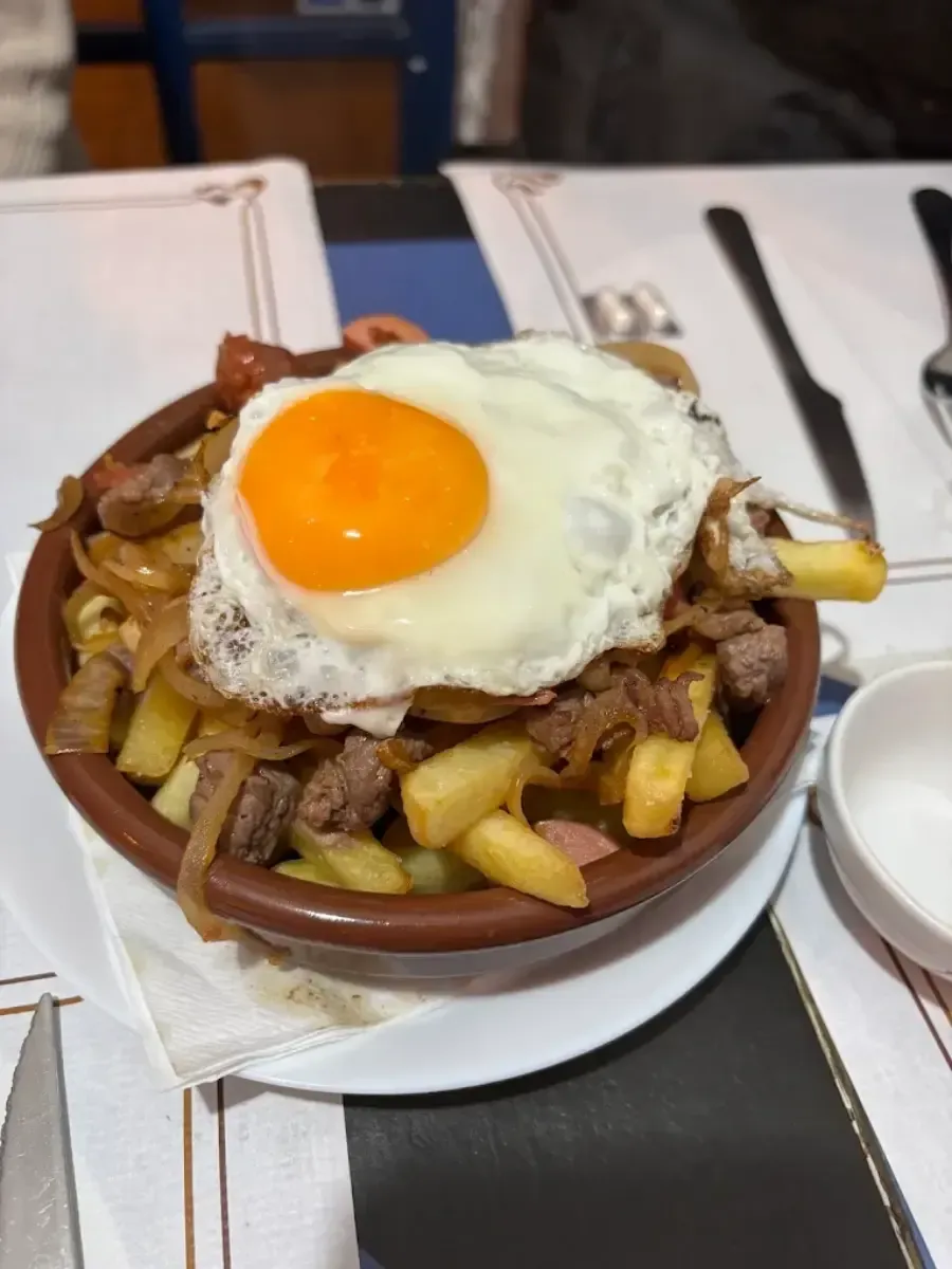 Bol de patatas fritas cubierto con carne picada y un huevo frito.