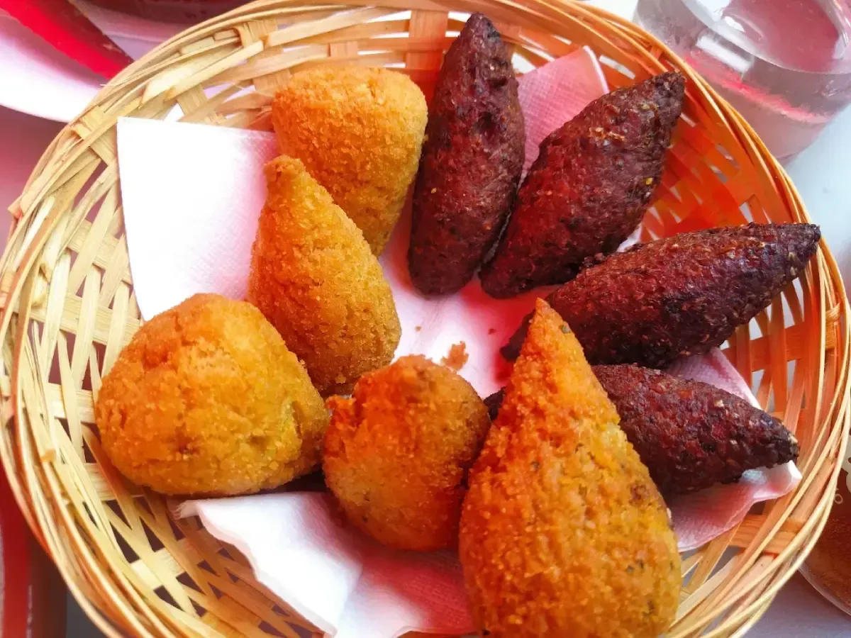 Cesta de aperitivos fritos variados en colores dorado y marrón oscuro sobre papel blanco.