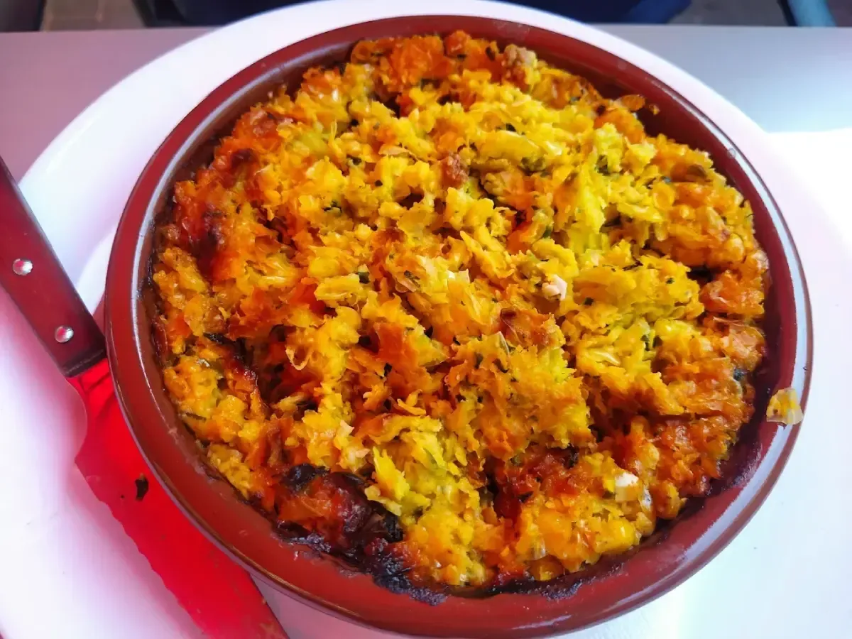 Cazuela horneada en una fuente roja, cubierta con migas doradas y naranjas sobre un plato blanco.