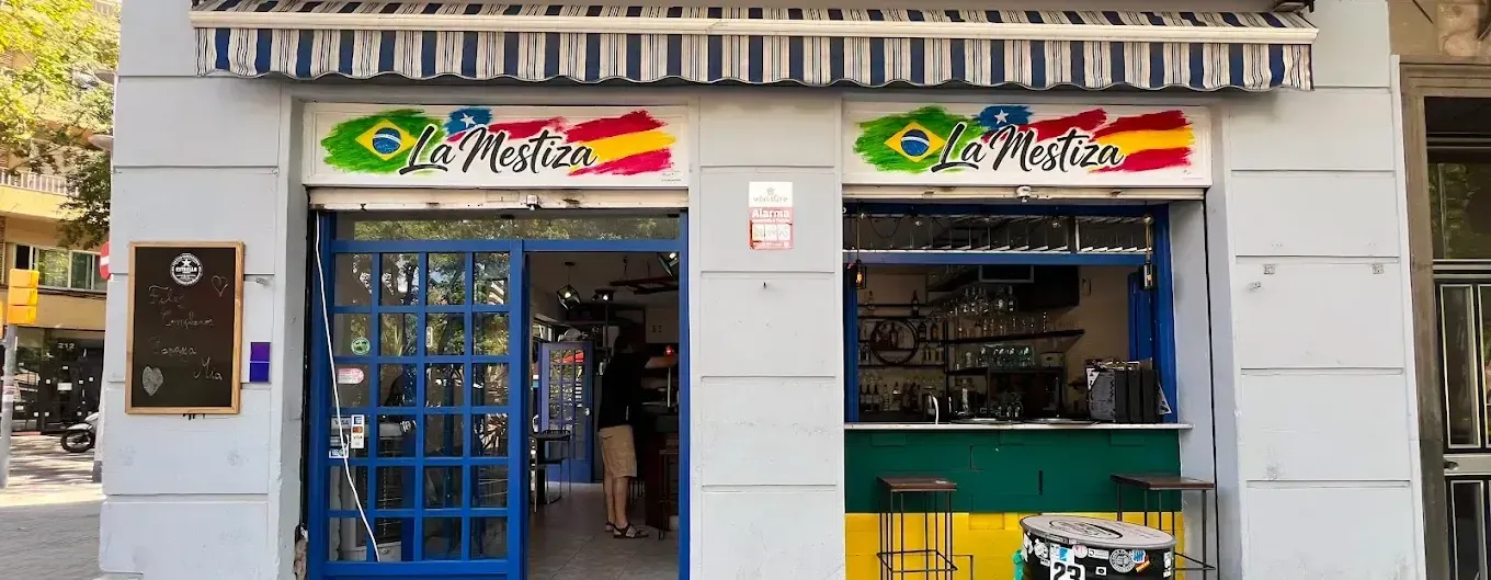 Pequeña tienda con puerta azul y ventanilla de atención al público verde bajo toldos a rayas.