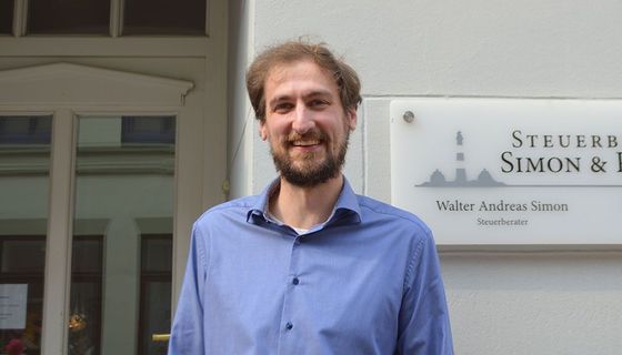 Ein Mann in einem blauen Hemd steht vor einem Schild mit der Aufschrift „Steuerb Simon & I“.