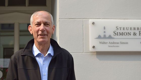 Ein Mann steht vor einem Schild mit der Aufschrift „Steuerbe Simon & F“