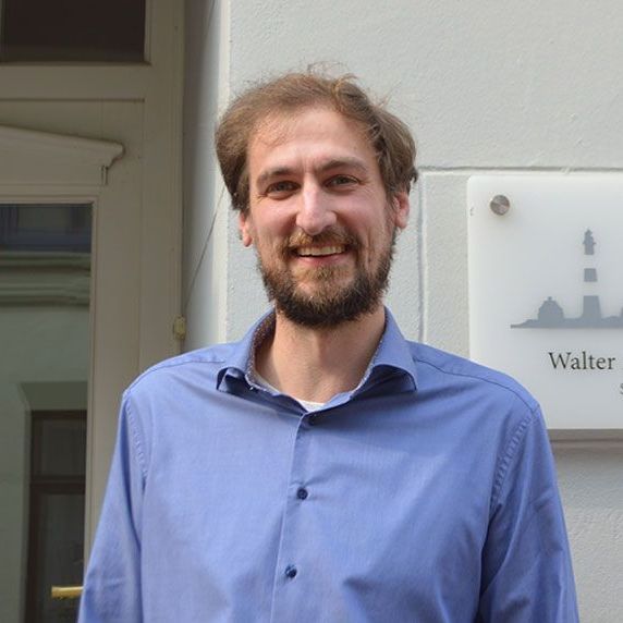 Ein Mann in einem blauen Hemd steht vor einem Schild mit der Aufschrift „Walter“