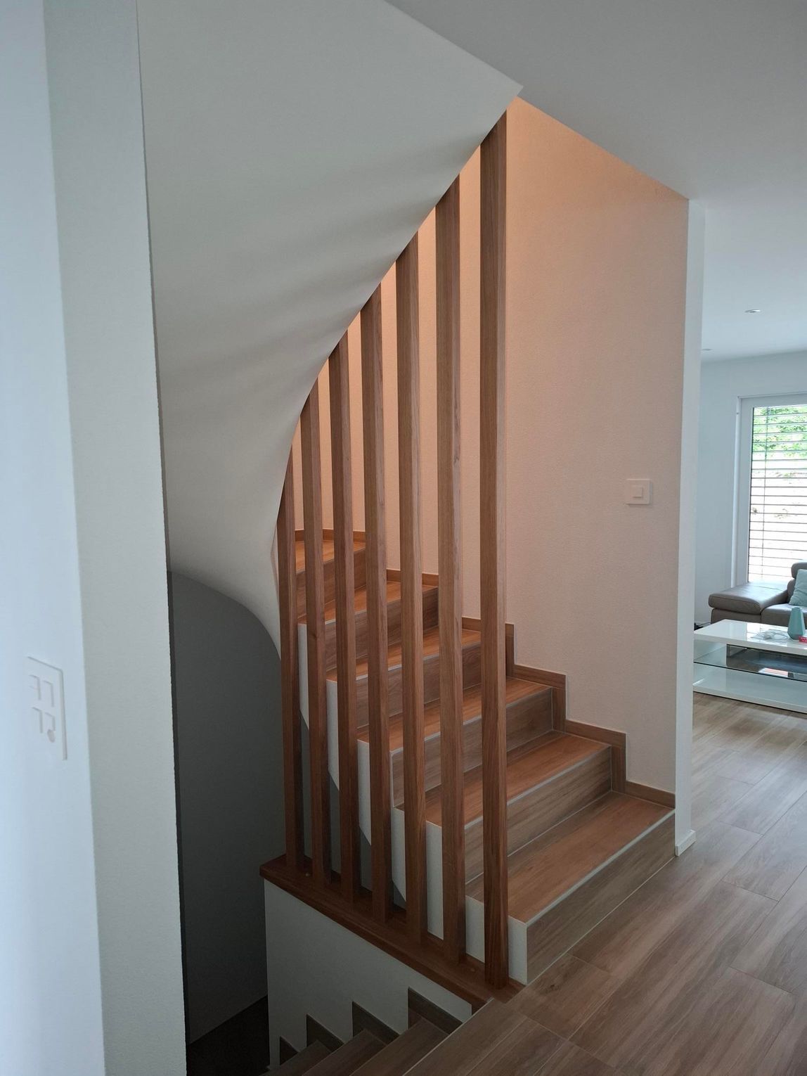 Escalier en bois avec rampes verticales en bois contre un mur blanc.