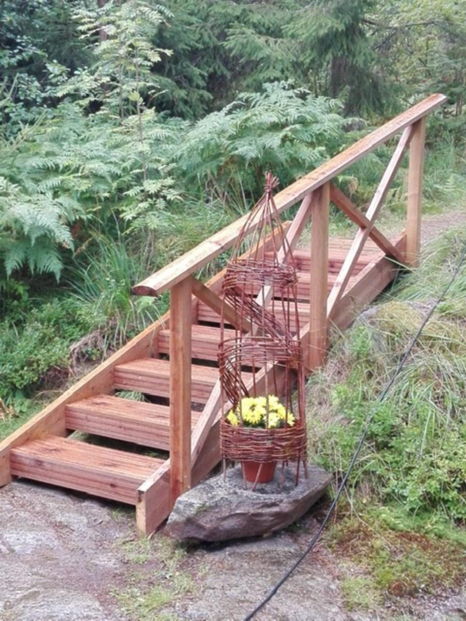 Puinen portaikko, jossa on kaide, metsäisellä alueella. Kukkakori koristaa portaita.