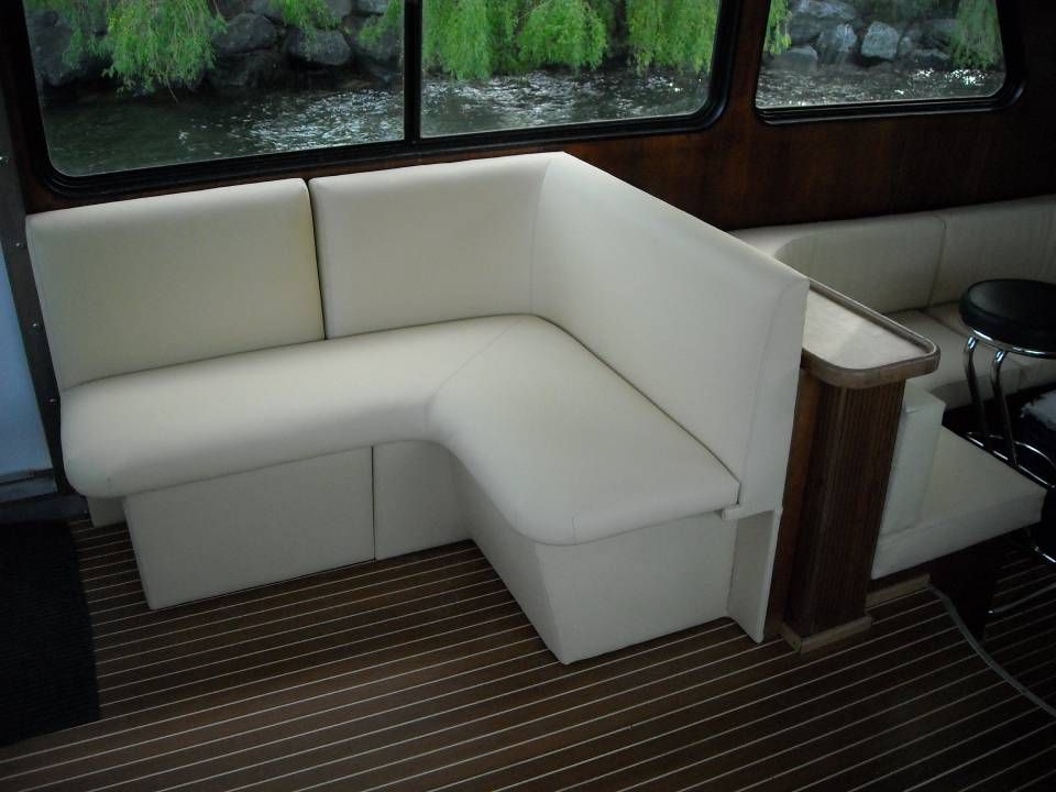 Divano angolare color crema all'interno della cabina di una barca, con finiture in legno e moquette a righe.