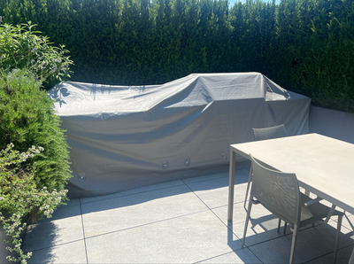 Elegante patio esterno con divano bianco imbottito, cuscini decorati e tavolo con piano in vetro e decorazioni verdi.