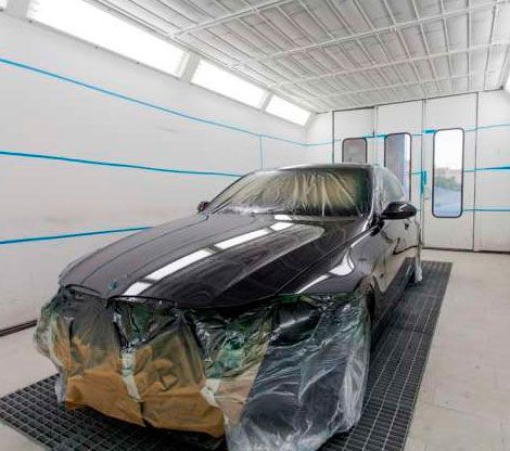 Un coche negro está estacionado en una cabina de pintura cubierto de plástico.