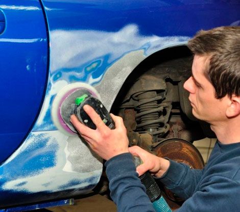 Un hombre está lijando un coche azul con una lijadora.