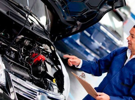 Un hombre mira debajo del capó de un coche mientras sostiene un portapapeles.
