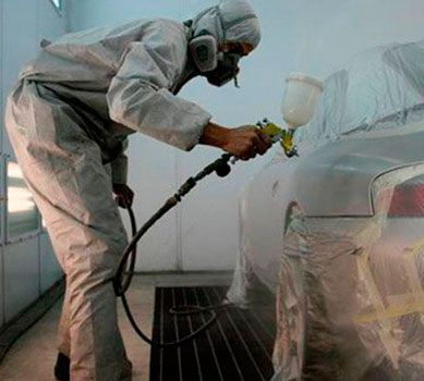 Un hombre está pintando con aerosol un coche en una cabina de pintura.